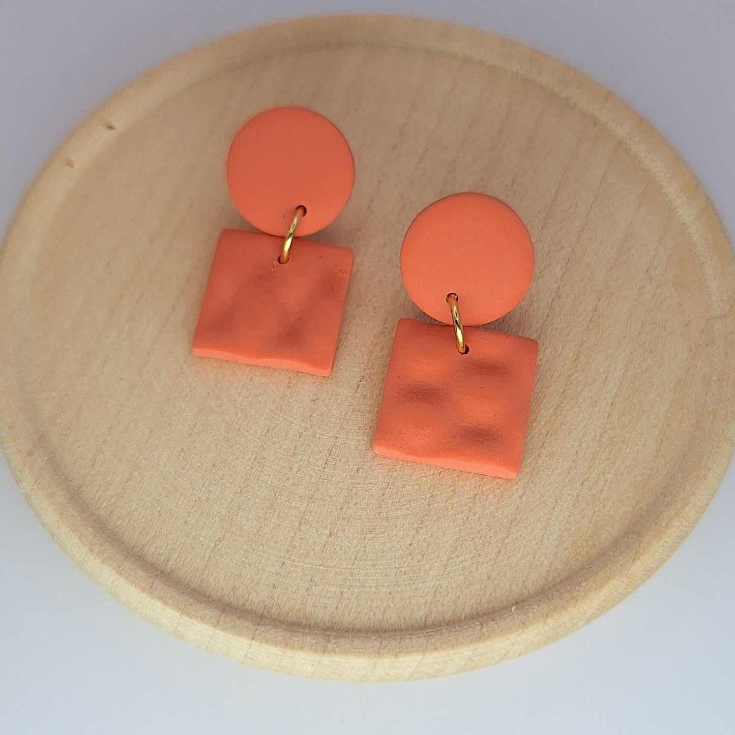 Orange earrings on a wooden plate with a light gray background