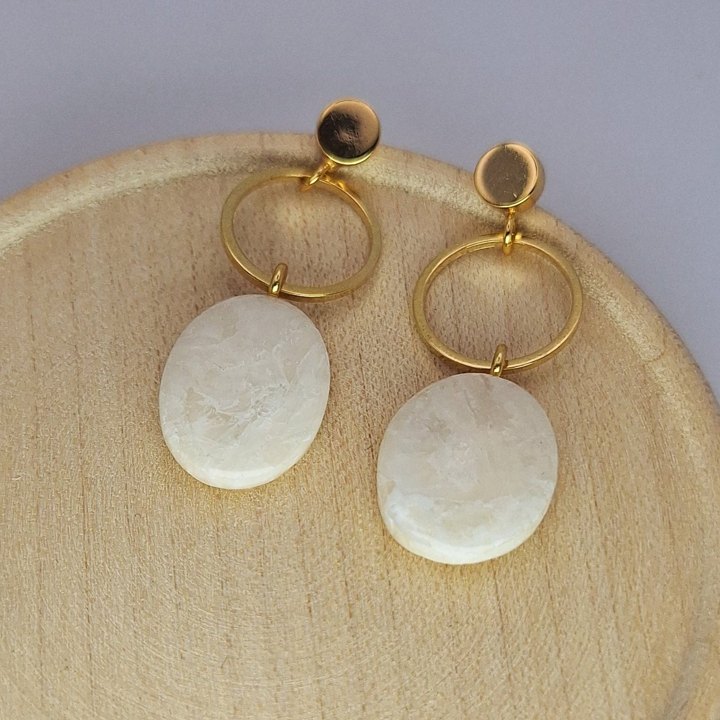 Pair of earrings with gold loops and white stones on a wooden plate.