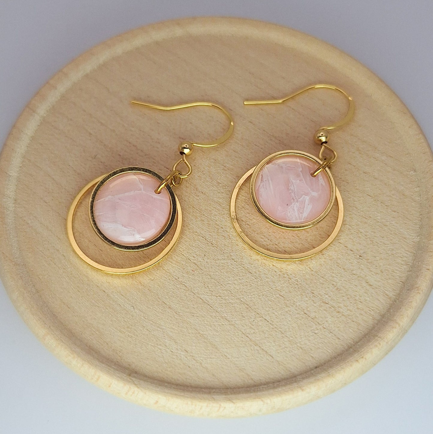 Gold earrings with pink stones on a wooden plate