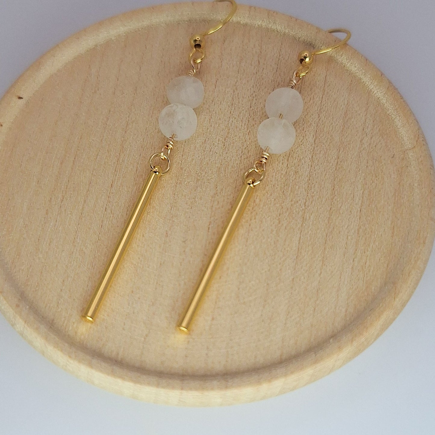 Pair of gold earrings with white beads on a wooden plate.