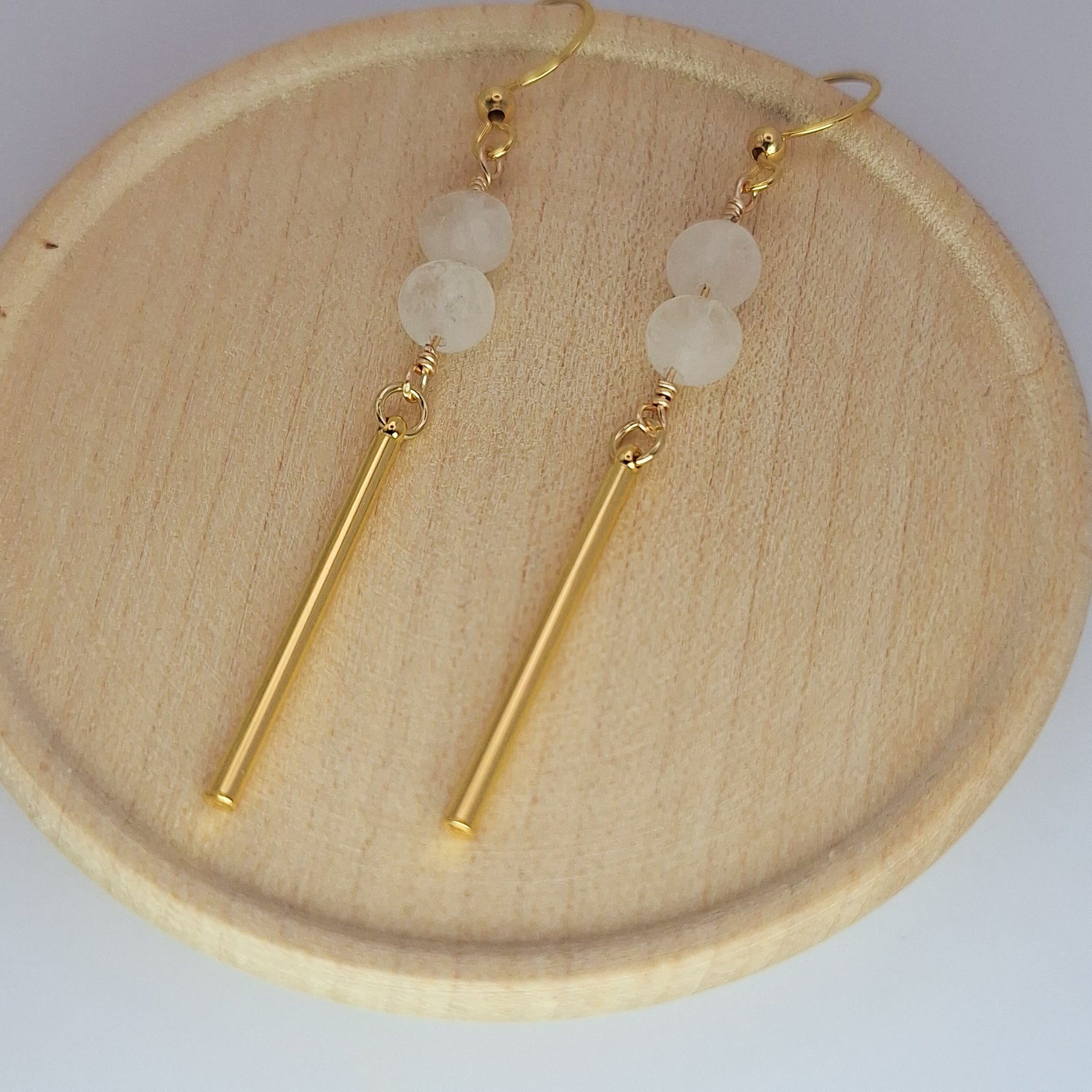 Pair of gold earrings with white beads on a wooden plate.