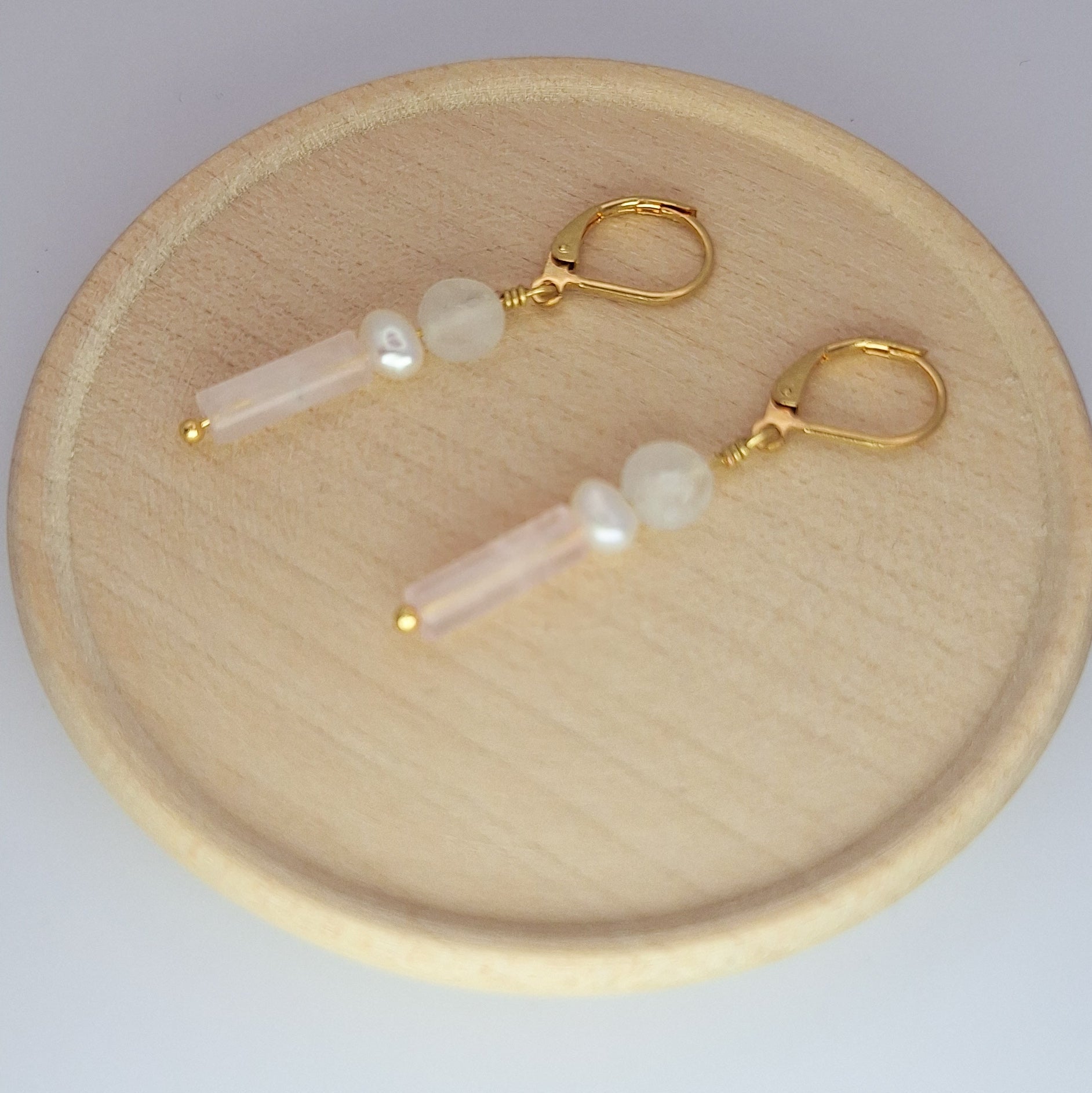 Pair of earrings with gold hooks and pearl-like beads on a wooden plate.