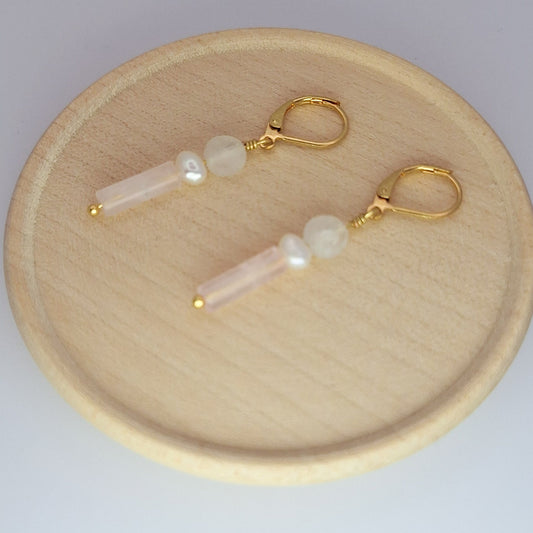 Pair of earrings with gold hooks and pearl-like beads on a wooden plate.